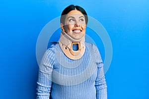 Beautiful brunette woman wearing cervical collar looking away to side with smile on face, natural expression