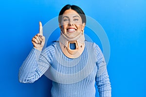 Beautiful brunette woman wearing cervical collar pointing finger up with successful idea