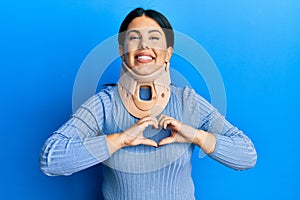 Beautiful brunette woman wearing cervical collar smiling in love showing heart symbol and shape with hands