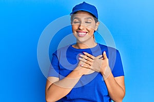 Beautiful brunette woman wearing delivery uniform smiling with hands on chest with closed eyes and grateful gesture on face