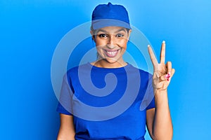 Beautiful brunette woman wearing delivery uniform smiling with happy face winking at the camera doing victory sign