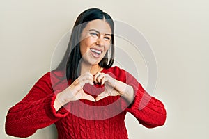 Beautiful brunette woman wearing wool winter sweater smiling in love doing heart symbol shape with hands