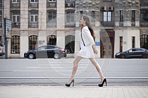 Beautiful brunette woman in white dress walking on the street