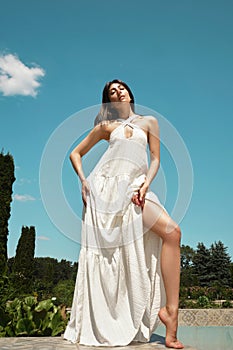 Beautiful brunette woman in a white summer dress on the background of the sky and nature.