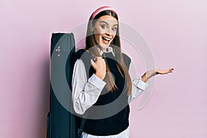 Beautiful brunette young musician woman wearing guitar case celebrating achievement with happy smile and winner expression with