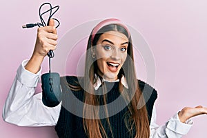 Beautiful brunette young woman holding computer mouse device celebrating achievement with happy smile and winner expression with