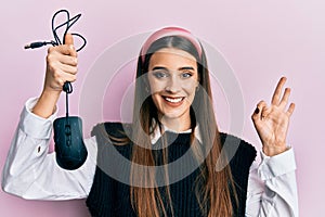 Beautiful brunette young woman holding computer mouse device doing ok sign with fingers, smiling friendly gesturing excellent