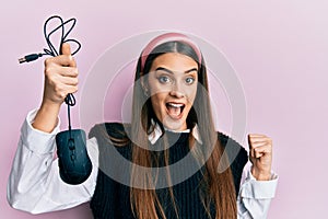 Beautiful brunette young woman holding computer mouse device pointing thumb up to the side smiling happy with open mouth