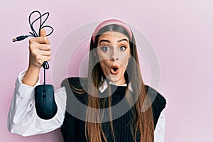 Beautiful brunette young woman holding computer mouse device scared and amazed with open mouth for surprise, disbelief face