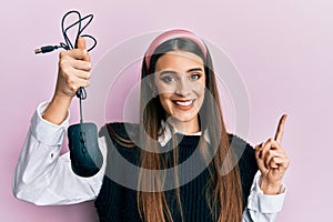 Beautiful brunette young woman holding computer mouse device smiling happy pointing with hand and finger to the side