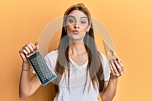 Beautiful brunette young woman holding grater and cheese looking at the camera blowing a kiss being lovely and sexy