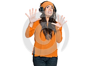 Beautiful brunette young woman listening to music using headphones afraid and terrified with fear expression stop gesture with
