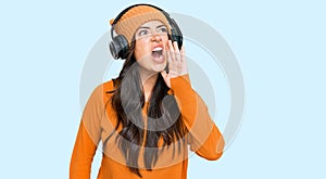 Beautiful brunette young woman listening to music using headphones shouting and screaming loud to side with hand on mouth