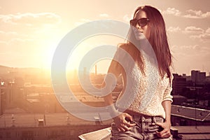 Beautiful brunette young woman posing above sunset city background