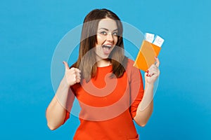 Beautiful brunette young woman wearing red orange dress hol in hand passport tickets isolated over trendy blue wall