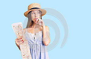 Beautiful brunette young woman wearing summer hat holding city map serious face thinking about question with hand on chin,