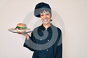 Beautiful brunettte woman chef holding burguer looking positive and happy standing and smiling with a confident smile showing