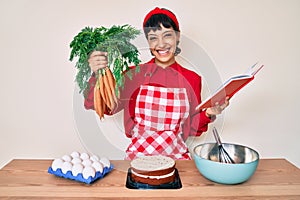 Beautiful brunettte woman cooking carrot cake reading recipes book smiling with a happy and cool smile on face