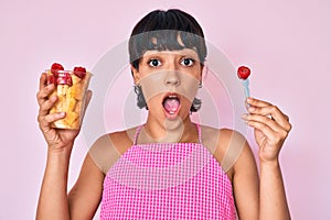 Beautiful brunettte woman eating fresh and healthy fruit afraid and shocked with surprise and amazed expression, fear and excited