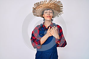 Beautiful brunettte woman wearing farmer clothes smiling with hands on chest with closed eyes and grateful gesture on face