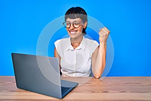 Beautiful brunettte woman working using computer laptop screaming proud, celebrating victory and success very excited with raised