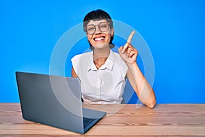 Beautiful brunettte woman working using computer laptop surprised with an idea or question pointing finger with happy face, number