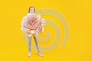 Beautiful bud. Cute girl holding a huge peony flower in her hands on a yellow background
