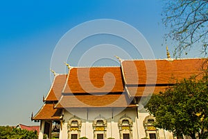 Beautiful Buddhist church, ubosot sanctuary hall with its expansive orange tiles roof under blue sky. Orange and red roof tiles at