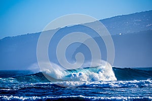 Beautiful and bug wave is breaking on the sea or ocean - blue water and pacific or athlantic - houses and mountains at the