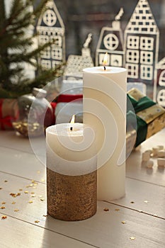 Beautiful burning candles with Christmas decor on white wooden table near window