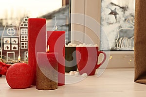 Beautiful burning candles with Christmas decor on white wooden table near window, space for text