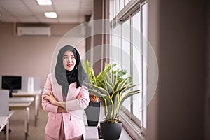 Beautiful business asian woman wearing hijab while standing and looking on window in the office
