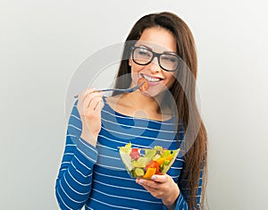 Beautiful business happy woman in blue clothing and eye glasses eating green healthy food with funny face on blue background