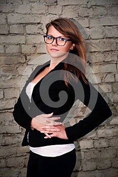 Beautiful business woman in a black suit and glasses on a brick wall background concept of a strong and successful female leader