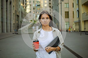 Beautiful business woman is going to work with coffee walking near office buildings. Portrait of a successful business woman holdi