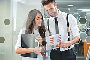Beautiful business woman and handsome man discussing financial graphs while standing in modern office.
