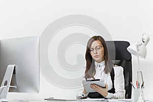 Beautiful business woman in suit and glasses working at computer with documents in light office