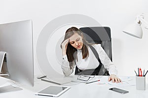 Beautiful business woman in suit and glasses working at computer with documents in light office