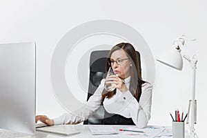 Beautiful business woman in suit and glasses working at computer with documents in light office