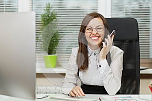 Beautiful business woman in suit and glasses working at computer with documents in light office