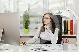 Beautiful business woman in suit and glasses working at computer with documents in light office