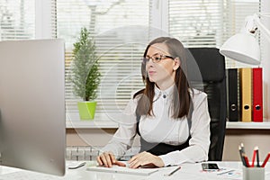 Beautiful business woman in suit and glasses working at computer with documents in light office