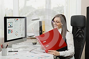 Beautiful business woman in suit and glasses working at computer with documents in light office