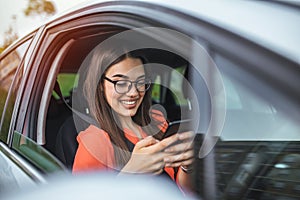 Beautiful business woman is using a smart phone and smiling while sitting on front seat in the car. Portrait of beautiful smiling