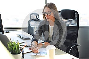 Beautiful business woman is writing something down while sitting in the office desk