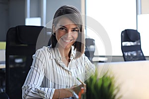 Beautiful business woman is writing something down while sitting in the office desk