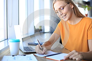 Beautiful business woman is writing something down while sitting in the office desk