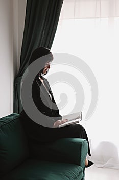 Beautiful business woman writing something in the note pad while sitting on the sofa at office, charming brunette female