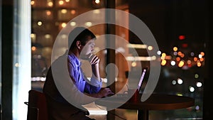 Beautiful businessman working overtime at night in executive office. City lights are visible in background from a large