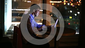 Beautiful businessman working overtime at night in executive office. City lights are visible in background from a large